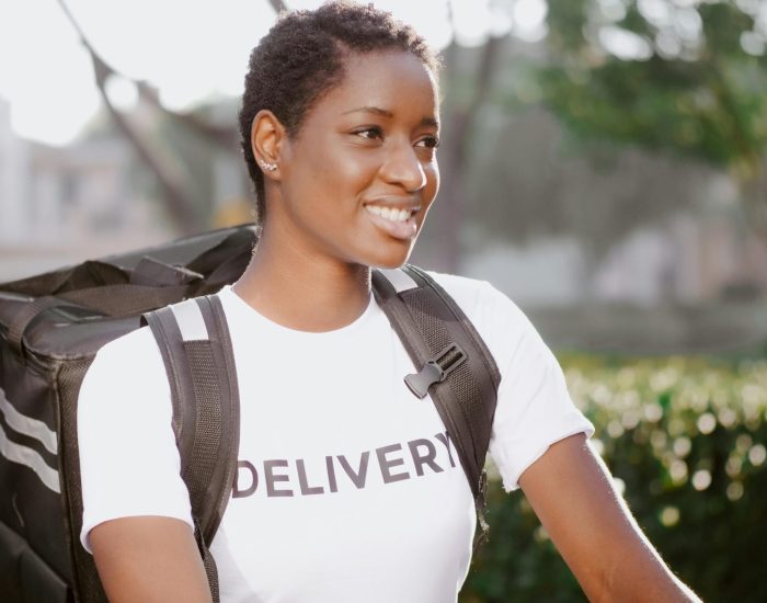 African American woman smiling with delivery backpack outdoors in daylight.