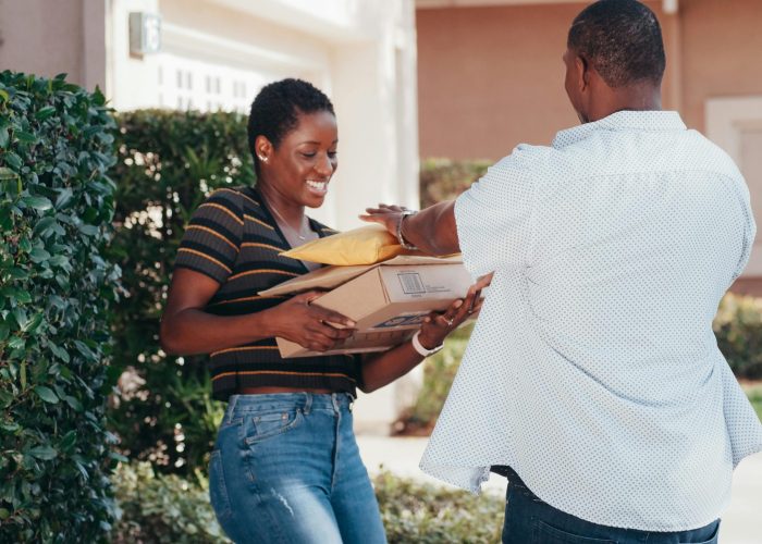 A smiling woman receives multiple packages from a delivery man outdoors.